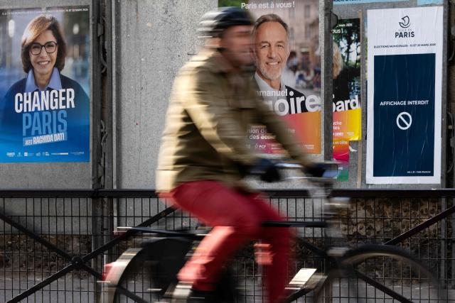 A cyclist rides past billboards displaying campaign posters of mayoral candidates during the second round of the municipal elections in Paris on March 22, 2026. (Photo by JOEL SAGET / AFP)