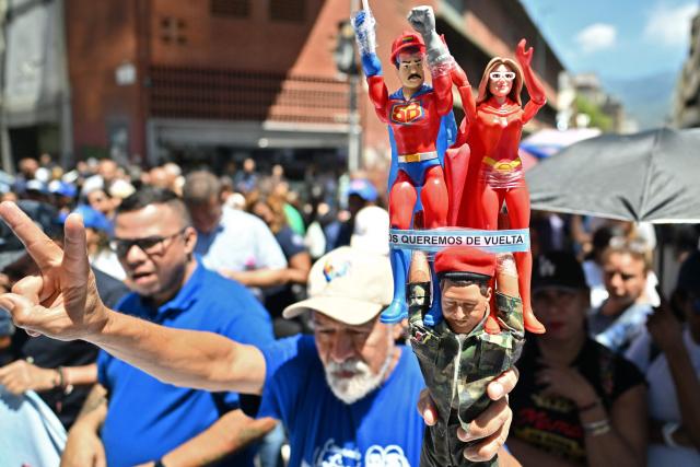 A man flashes the V sign as he holds up toys depicting Venezuelan deposed president Nicolas Maduro and his wife Cilia Flores, during a march demanding the complete lifting of US sanctions in Caracas on March 23, 2026. (Photo by Juan BARRETO / AFP)