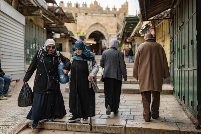 Palestinian women help one another down stone steps in Jerusalem's Old City on March 23, 2026. Since the United States and Israel unleashed strikes on Iran on February 28, war has spread across the Middle East, with casualties reported in countries across the region. (Photo by Odd ANDERSEN / AFP) / 