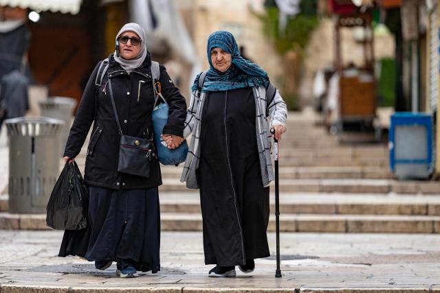 Palestinian women help one another down stone steps in Jerusalem's Old City on March 23, 2026. Since the United States and Israel unleashed strikes on Iran on February 28, war has spread across the Middle East, with casualties reported in countries across the region. (Photo by Odd ANDERSEN / AFP) / 
