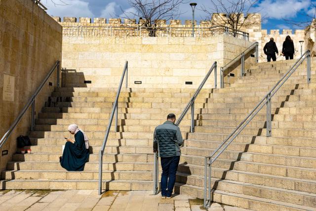 A Palestinian woman (L) and a Jewish man check their smartphones on the steps leading to Jaffa Gate in Jerusalem's Old City on March 23, 2026. Since the United States and Israel unleashed strikes on Iran on February 28, war has spread across the Middle East, with casualties reported in countries across the region. (Photo by Odd ANDERSEN / AFP) / 