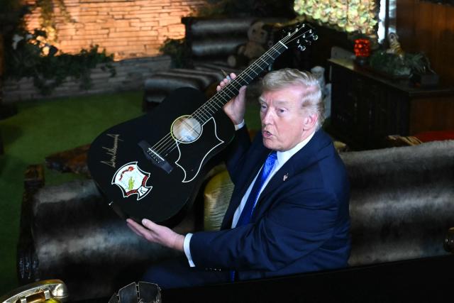 US President Donald Trump shows a replica of one of Elvis Presley's guitars after he signed it, as he tours the Jungle Room during his visit to Graceland in Memphis, Tennessee, on March 23, 2026. (Photo by SAUL LOEB / AFP)