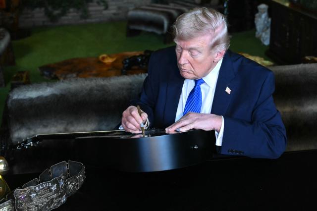 US President Donald Trump signs a replica of one of Elvis Presley's guitars, as he tours the Jungle Room during his visit to Graceland in Memphis, Tennessee, on March 23, 2026. (Photo by SAUL LOEB / AFP)