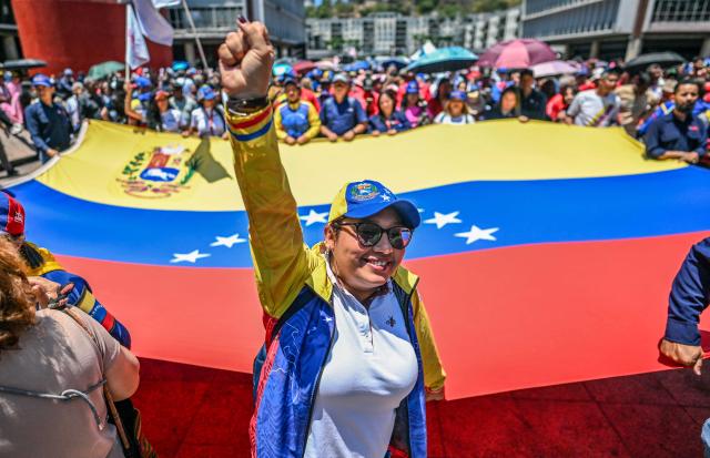 An activist raises her fist while holding a huge Venezuelan flag during a march demanding the complete lifting of US sanctions, in Caracas, on March 23, 2026. (Photo by Juan BARRETO / AFP)