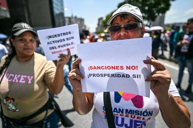 A woman holds a sign reading "Sanctions no, prosperity yes!" during a march demanding the complete lifting of US sanctions in Caracas on March 23, 2026. (Photo by Juan BARRETO / AFP)