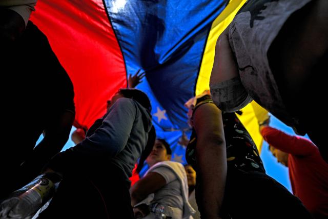 People walk under a huge Venezuelan flag during a march demanding the complete lifting of US sanctions in Caracas on March 23, 2026. (Photo by Juan BARRETO / AFP)