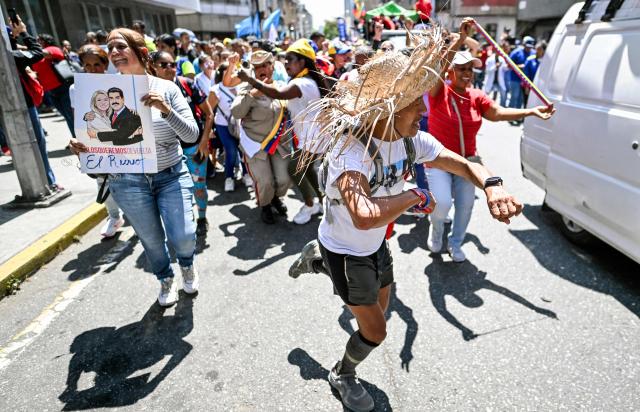 People dance while taking part in a march demanding the complete lifting of US sanctions, in Caracas, on March 23, 2026. (Photo by Juan BARRETO / AFP)