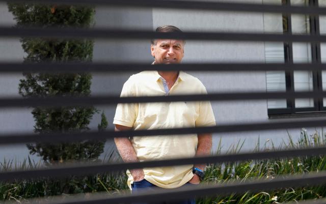 (FILES) Former Brazilian President Jair Bolsonaro gestures from his residence in Brasilia on September 3, 2025. Former Brazilian President Jair Bolsonaro, who was hospitalized with bronchopneumonia, was released from intensive care on March 23, 2026, one of his doctors reported, as he awaits the Supreme Court’s decision on whether to grant him house arrest. (Photo by Sergio Lima / AFP)