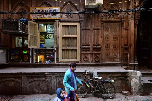 This photograph taken on February 5, 2026 shows a woman walking past a century-old haveli in the old quarters of Delhi. Once the grand residences of Mughal-era nobility, the Indian capital's haveli homes now stand at fragile crossroads -- a handful lovingly restored but many more sliding quietly into ruin. (Photo by Manan VATSYAYANA / AFP)