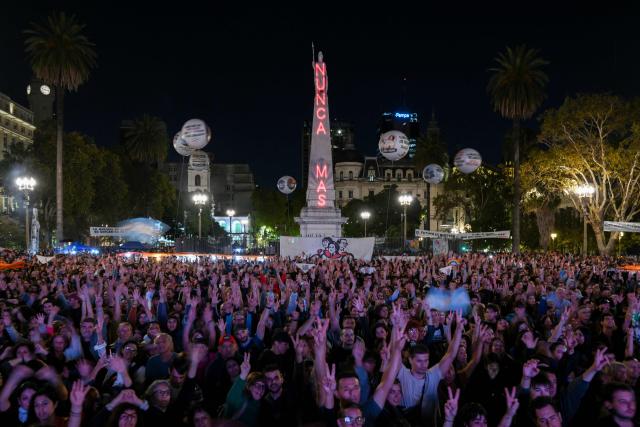 TOPSHOT - People gather in the Plaza de Mayo square in Buenos Aires on March 23, 2026, with the Piramide de Mayo monument in the background illuminated with the phrase "Never Again" to attend a vigil one day before the 50th anniversary of the military coup that ushered in the military dictatorship (1976–1983). (Photo by Luis ROBAYO / AFP)