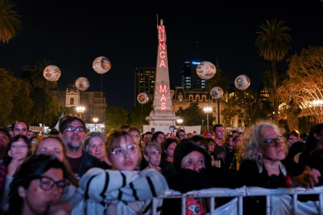 People gather in the Plaza de Mayo square in Buenos Aires on March 23, 2026, with the Piramide de Mayo monument in the background illuminated with the phrase "Never Again" to attend a vigil one day before the 50th anniversary of the military coup that ushered in the military dictatorship (1976–1983). (Photo by Luis ROBAYO / AFP)
