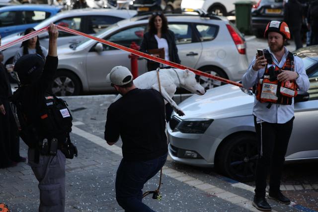 A man carrying a dog leaves the site of an Iranian missile strike in Tel Aviv on March 24, 2026. First responders said six people were injured on March 24 in Israel's commercial hub Tel Aviv, where police reported several impact sites after the military warned of incoming missile fire from Iran. Iran launched a new wave of missiles against Israel on March 24, hours after US President Donald Trump hailed "very good" talks to end the war despite Tehran denying any dialogue had taken place. (Photo by Jack GUEZ / AFP) / 