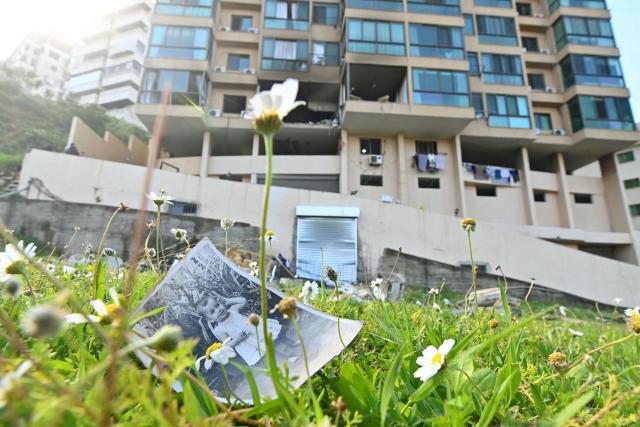 An old family photograph lies on the grass outside a damaged building following an overnight Israeli airstrike that targeted an apartment in Bshamoun, southeast of Beirut, on March 24, 2026. An Israeli strike on Bshamoun killed two people, Lebanon's health ministry said, while strikes on the capital's southern suburbs continued throughout the night. Located in the mountainous, Druze-majority Aley district southeast of Beirut, Bshamoun lies outside of Hezbollah's traditional strongholds. (Photo by FADEL itani / AFP)