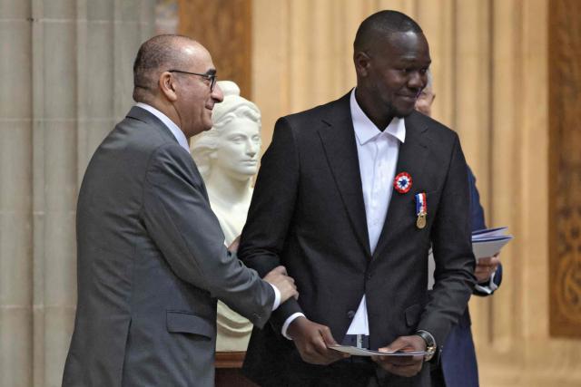Fousseynou Cisse (R) is congratulated by France's Interior Minister Laurent Nunez after receiving his naturalization certifcate during a at the Pantheon in Paris on March 24, 2026. Cisse, a 39-year-old Senegalese man, rescued six people—four children and their two mothers from a fire in their apartment in Paris on July 4, 2025. The rescue, filmed by a resident, quickly went viral on social media. (Photo by Ludovic MARIN / AFP)