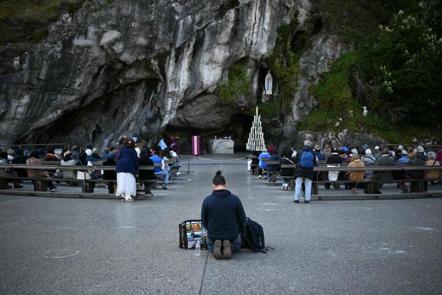 A pilgrim is kneeling in prayer before the Grotto of Massabielle during a mass at the Shrine of Lourdes on March 24, 2026. (Photo by LIONEL BONAVENTURE / AFP)