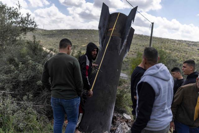 A Palestinian man measures an Iranian missile fragment that landed in the Israeli-occupied West Bank village of Hares on March 24, 2026. Since the United States and Israel unleashed strikes on Iran on February 28, war has spread across the Middle East, with casualties reported in countries across the region. (Photo by Ilia YEFIMOVICH / AFP) / 