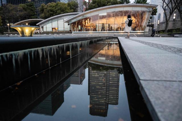 A woman takes a photo of the architecture at the Kokyo Gaien National Garden as an office building is reflected in a water feature, in Tokyo on March 24, 2026. (Photo by Andrew CABALLERO-REYNOLDS / AFP)