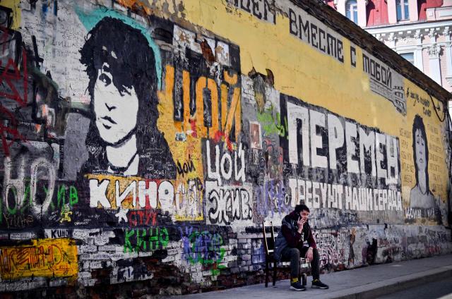 A man sits in front of the "Tsoi Wall", a memorial to Viktor Tsoi - the Soviet rock idol who has died in a car crash on August 15, 1990, in downtown Moscow on March 24, 2026. The inscription on the wall reads: "Our Hearts Demand Changes!". This song was one of the most popular anthems of social and political protests in Russia for decades. (Photo by Alexander NEMENOV / AFP)
