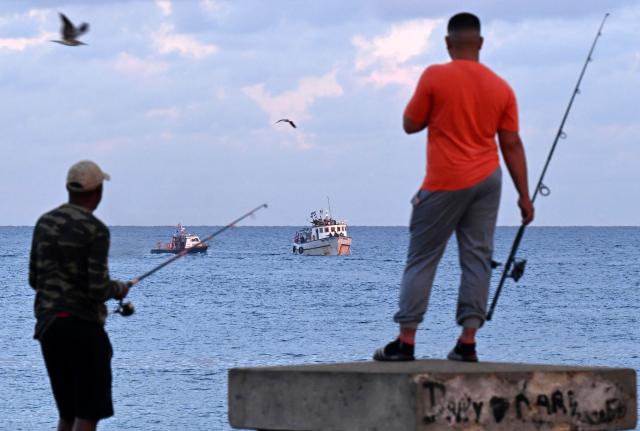 Men fish as the vessel Maguro, arriving from Mexico with humanitarian aid as part of the Nuestra America convoy, docks at the port of Havana on March 24, 2026. (Photo by YAMIL LAGE / AFP)