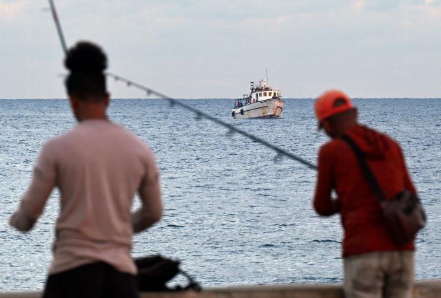 Men fish as the vessel Maguro, arriving from Mexico with humanitarian aid as part of the Nuestra America convoy, docks at the port of Havana on March 24, 2026. (Photo by YAMIL LAGE / AFP)