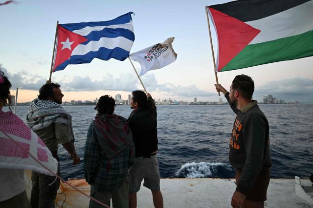 Activists wave Cuban and Palestinian flags on board the vessel Maguro as it arrives from Mexico with humanitarian aid as part of the Nuestra America convoy, docking at the port of Havana on March 24, 2026. The first boat of a flotilla carrying medical supplies, food and solar panels reached Cuba on March 24, 2026 to aid the island as a US fuel blockade deepens its energy crisis. The Maguro shrimp fishing boat docked in Havana three days later than hoped after battling strong winds, currents and a pesky battery, with two other ships due to follow. (Photo by YURI CORTEZ / AFP)