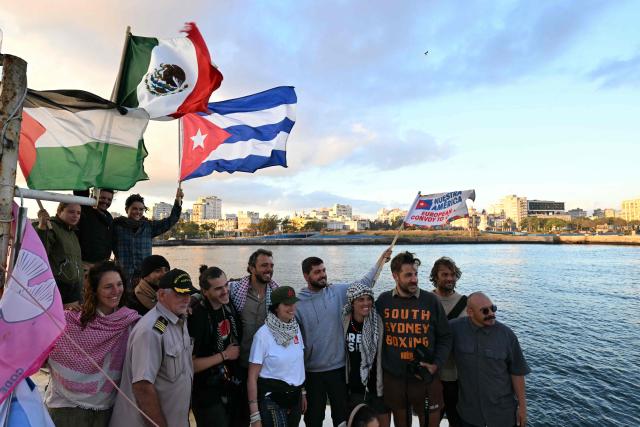 Activists pose wuth Cuban, Mexican and Palestinian flags on board the vessel Maguro as it arrives from Mexico with humanitarian aid as part of the Nuestra America convoy, docking at the port of Havana on March 24, 2026. The first boat of a flotilla carrying medical supplies, food and solar panels reached Cuba on March 24, 2026 to aid the island as a US fuel blockade deepens its energy crisis. The Maguro shrimp fishing boat docked in Havana three days later than hoped after battling strong winds, currents and a pesky battery, with two other ships due to follow. (Photo by YURI CORTEZ / AFP)