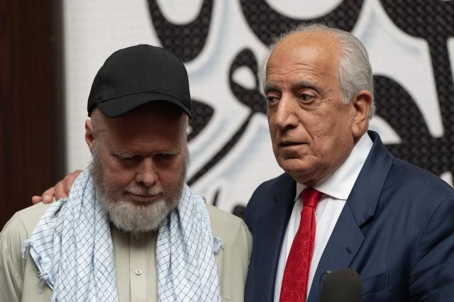 US citizen Dennis Coyle (L) upon his release by the Taliban, addresses the media with US former special envoy to Afghanistan Zalmay Khalilzad (R) at the airport in Kabul on March 24, 2026. Afghanistan's Taliban government announced on March 24 that it was freeing a US national who had been detained for more than a year. The foreign ministry said the family of linguist and researcher Dennis Coyle had written to the supreme leader of Afghanistan, requesting his release for Eid. (Photo by Wakil KOHSAR / AFP)