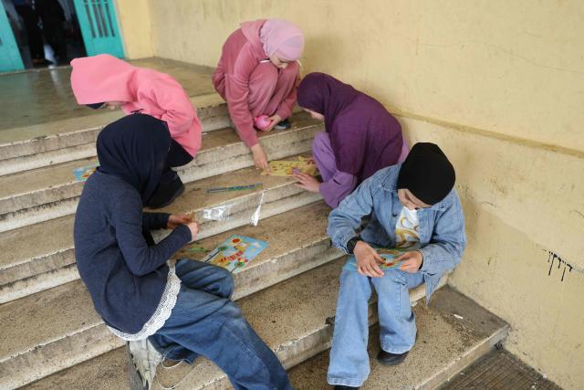 Displaced Lebanese girls spend time coloring as they sits on the stairs at a public school turned into a shelter in the town of Dekwaneh, north of Beirut on March 24, 2026. Lebanon was pulled into the Middle East war when the Tehran-backed Hezbollah militant group began firing rockets into Israel on March 2 to avenge the killing of Iran's supreme leader on February 28 by the US and Israel. Israel has since launched strikes across Lebanon, killing at least 1,039 people and displacing more than a million others in more than three weeks of fighting. It has also sent ground troops into the country's south. (Photo by Anwar AMRO / AFP)