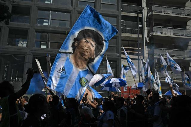 People with a flag depicting late Argentinian football star Diego Maradona, take part in a march to Plaza de Mayo aquare in Buenos Aires on March 24, 2026, on the 50th anniversary of the beginning of the last military dictatorship. In Argentina, March 24th is a day of mourning, marches and political disputes. Fifty years on from the coup d’etat, thousands of people are taking to the streets again to commemorate the victims of a dictatorship that the government of far-right leader Javier Milei is seeking to rewrite. (Photo by Luis ROBAYO / AFP)