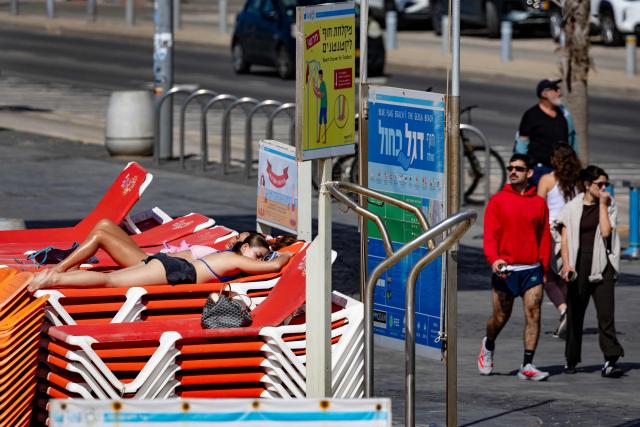 Two women sunbathe on top of a stack of sun beds on a largely empty beach in Tel Aviv on March 24, 2026. Iran fired a fresh broadside of missiles at Israel March 24, causing damage and injuries in Tel Aviv, as uncertainty swirled over possible talks to end the three-week Middle East war. (Photo by Odd ANDERSEN / AFP) / 