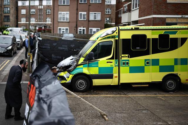 A member (L) of the Jewish community views the scene of an antisemitic arson attack through a makeshift fence in the Golders Green neighbourhood of north London, on March 24, 2026, a day after volunteer ambulances run by a Jewish organisation were set on fire. London's police chief pledged on March 23 over 250 more officers and "highly visible" armed patrols to protect the Jewish community after an arson attack on four volunteer ambulances run by a Jewish organisation next to a synagogue. (Photo by Henry NICHOLLS / AFP)