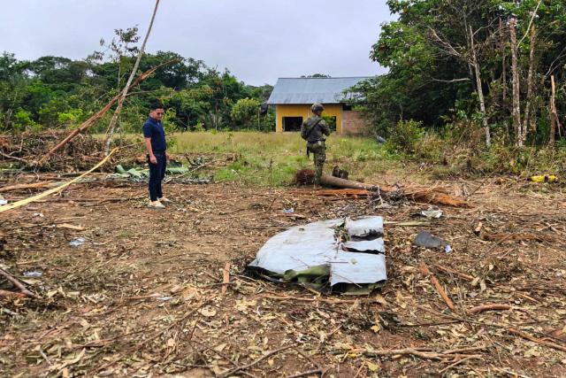A soldier and another man stand near debris of the Air Force Hercules that crashed during takeoff in Puerto Leguizamo, Colombia, near the southern border with Ecuador, on March 24, 2026. A Colombian military plane carrying 125 soldiers and crew members crashed on takeoff early on March 23, killing at least 66 people and injuring dozens more, officials said. (Photo by daniel ortiz / AFP)