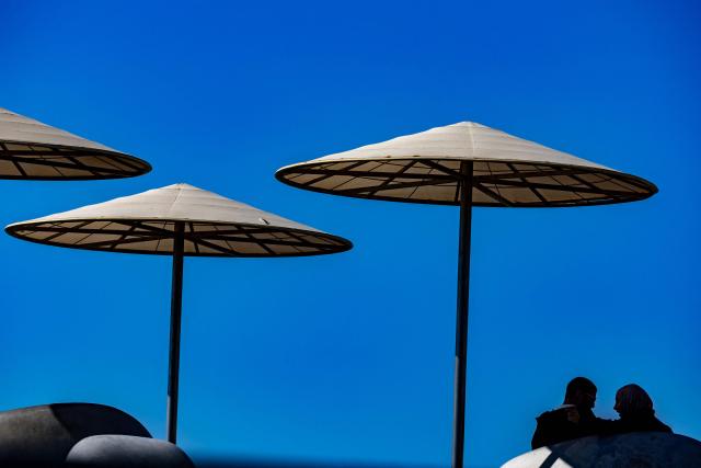 Sun umbrellas provide shade for a couple on a largely empty beach in Tel Aviv on March 24, 2026. Iran fired a fresh broadside of missiles at Israel March 24, causing damage and injuries in Tel Aviv, as uncertainty swirled over possible talks to end the three-week Middle East war. (Photo by Odd ANDERSEN / AFP) / 