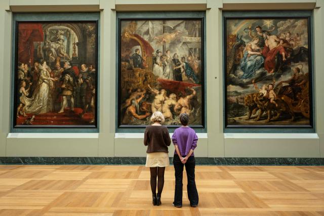 Employees look at paintings in The Medicis Gallery, in which are displayed 24 paintings by Flemish artist Peter Paul Rubens constituting the 'Marie de Medici Cycle', before their restoration, at Musee du Louvre in Paris on March 24, 2026. The Louvre has unveiled the details of an “exceptional operation” to restore the 24 paintings of the “Marie de’ Medici Cycle,” painted in the early 17th century by Rubens, one of the masters of Flemish painting. A call for tenders is underway to find two teams of restorers who will work simultaneously, starting in the autumn, on a project expected to last four years. (Photo by Blanca CRUZ / AFP)