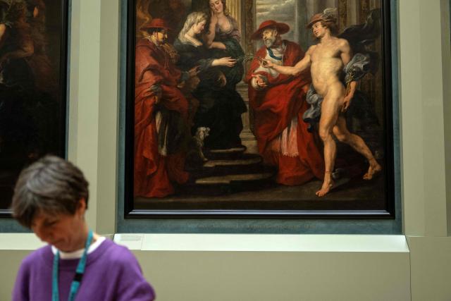 An employee walks past a painting in The Medicis Gallery, in which are displayed 24 paintings by Flemish artist Peter Paul Rubens constituting the 'Marie de Medici Cycle', before their restoration, at Musee du Louvre in Paris on March 24, 2026. The Louvre has unveiled the details of an “exceptional operation” to restore the 24 paintings of the “Marie de’ Medici Cycle,” painted in the early 17th century by Rubens, one of the masters of Flemish painting. A call for tenders is underway to find two teams of restorers who will work simultaneously, starting in the autumn, on a project expected to last four years. (Photo by Blanca CRUZ / AFP)