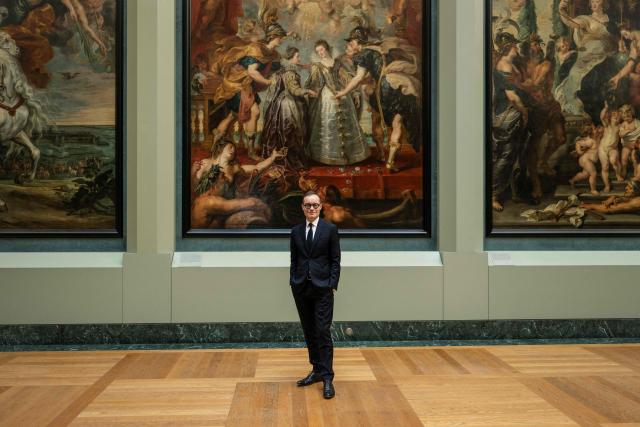 Director of the Paintings Department of Musee du Louvre Sebastien Allard poses next to "L'Echange des deux princesses de France et d'Espagne sur la Bidassoa a Hendaye" in The Medicis Gallery, in which are displayed 24 paintings by Flemish artist Peter Paul Rubens constituting the 'Marie de Medici Cycle', before their restoration, at Musee du Louvre in Paris on March 24, 2026. The Louvre has unveiled the details of an “exceptional operation” to restore the 24 paintings of the “Marie de’ Medici Cycle,” painted in the early 17th century by Rubens, one of the masters of Flemish painting. A call for tenders is underway to find two teams of restorers who will work simultaneously, starting in the autumn, on a project expected to last four years. (Photo by Blanca CRUZ / AFP)
