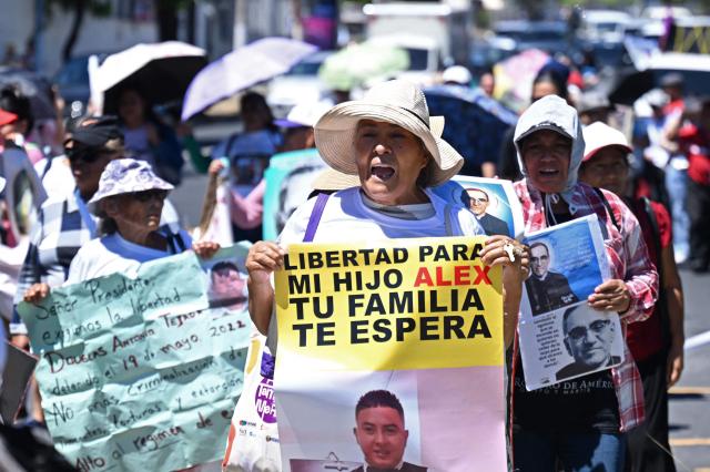 A woman holds a sign demanding her son's freedom and reading "Your family waits for you", during a protest against the emergency regime imposed by the government since March 2022, on the 46th anniversary of the assassination of Salvadoran Archbishop Oscar Arnulfo Romero (1917-1980) in San Salvador, on March 24, 2026. (Photo by Marvin RECINOS / AFP)