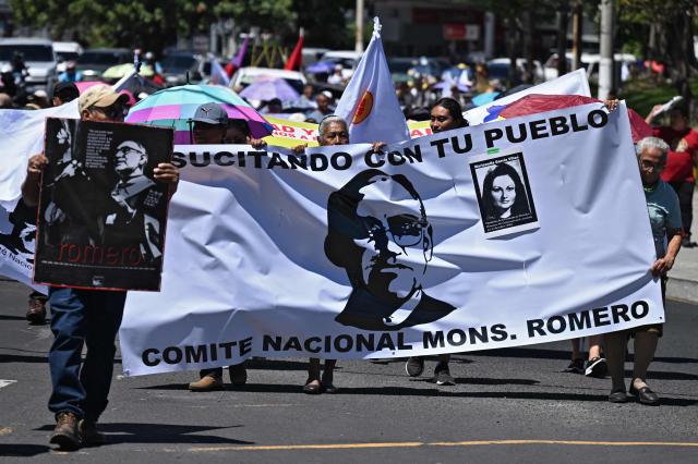People hold a banner depicting murdred Salvadoran Archbishop Oscar Arnulfo Romero (1917-1980) during a protest against the emergency regime imposed by the government since March 2022, on the 46th anniversary Romero's assassination, in San Salvador, on March 24, 2026. (Photo by Marvin RECINOS / AFP)