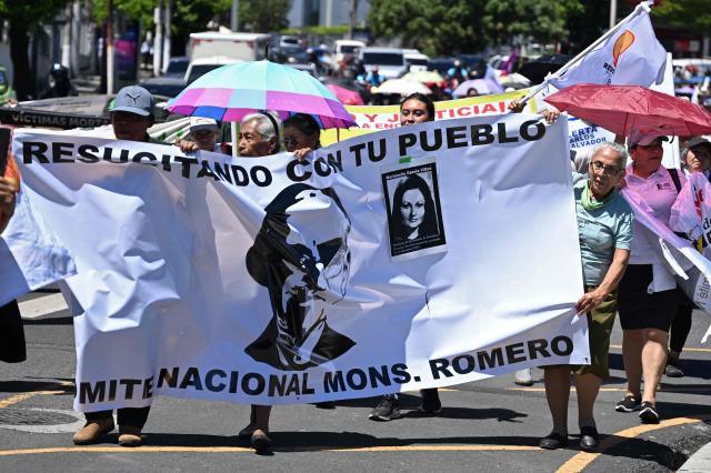 People hold a banner depicting murdred Salvadoran Archbishop Oscar Arnulfo Romero (1917-1980) during a protest against the emergency regime imposed by the government since March 2022, on the 46th anniversary Romero's assassination, in San Salvador, on March 24, 2026. (Photo by Marvin RECINOS / AFP)