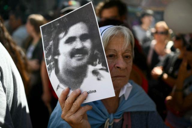 A woman holds up a portrait of a missing person during a march to Plaza de Mayo square in Buenos Aires on March 24, 2026, on the 50th anniversary of the beginning of the last military dictatorship. In Argentina, March 24th is a day of mourning, marches and political disputes. Fifty years on from the coup d’etat, thousands of people are taking to the streets again to commemorate the victims of a dictatorship that the government of far-right leader Javier Milei is seeking to rewrite. (Photo by Luis ROBAYO / AFP)