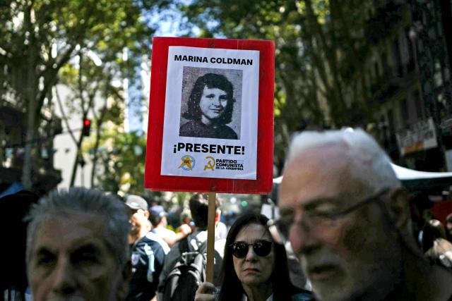A woman holds up a portrait of Marina Coldman during a march to Plaza de Mayo square in Buenos Aires on March 24, 2026, on the 50th anniversary of the beginning of the last military dictatorship. In Argentina, March 24th is a day of mourning, marches and political disputes. Fifty years on from the coup d’etat, thousands of people are taking to the streets again to commemorate the victims of a dictatorship that the government of far-right leader Javier Milei is seeking to rewrite. (Photo by Luis ROBAYO / AFP)