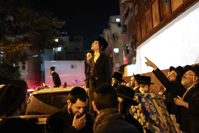 Ultra-Orthodox Jewish men and children look towards the damage at the site where a building was struck by a projectile in Bnei Brak, on the eastern outskirts of Tel Aviv, on March 24, 2026. The Middle East was sparked by joint US-Israeli strikes on Iran that triggered a wave of retaliatory missile and drone attacks against Israel and several other countries in the region. (Photo by Ilia YEFIMOVICH / AFP) / 