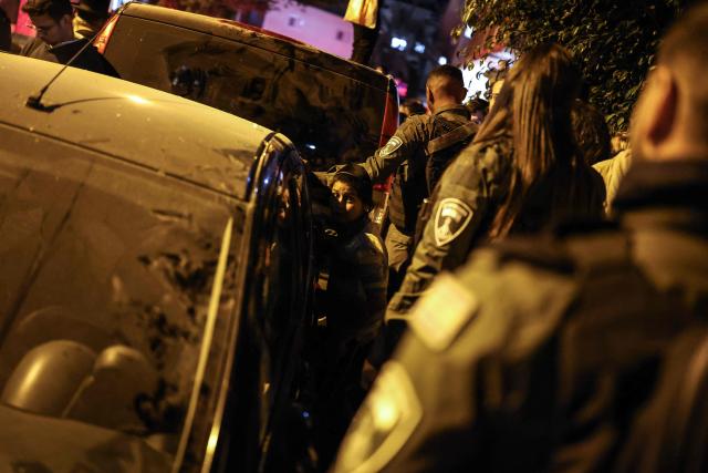 Security forces walk past a boy standing at the site where a building was struck by a projectile in Bnei Brak, on the eastern outskirts of Tel Aviv, on March 24, 2026. The Middle East was sparked by joint US-Israeli strikes on Iran that triggered a wave of retaliatory missile and drone attacks against Israel and several other countries in the region. (Photo by Ilia YEFIMOVICH / AFP) / 