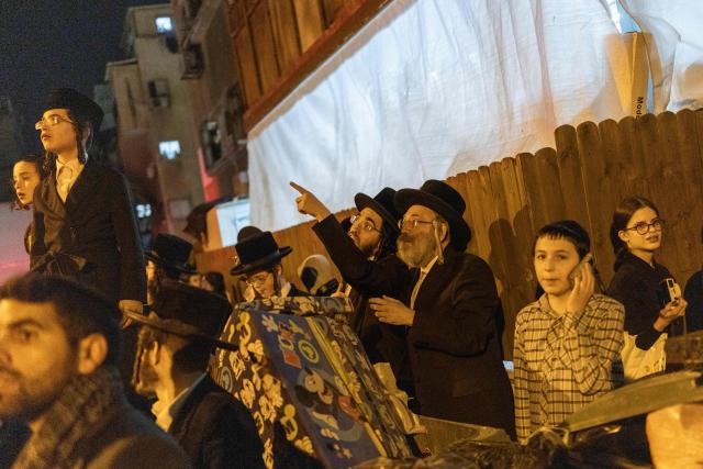 Members of the Ultra-Orthodox Jewish community look towards the damage at a site struck by a projectile in Bnei Brak, on the eastern outskirts of Tel Aviv, on March 24, 2026. The Middle East was sparked by joint US-Israeli strikes on Iran that triggered a wave of retaliatory missile and drone attacks against Israel and several other countries in the region. (Photo by Ilia YEFIMOVICH / AFP) / 
