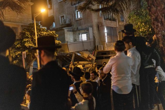 Members of the Ultra-Orthodox Jewish community look towards the damage at a site struck by a projectile in Bnei Brak, on the eastern outskirts of Tel Aviv, on March 24, 2026. The Middle East was sparked by joint US-Israeli strikes on Iran that triggered a wave of retaliatory missile and drone attacks against Israel and several other countries in the region. (Photo by Ilia YEFIMOVICH / AFP) / 