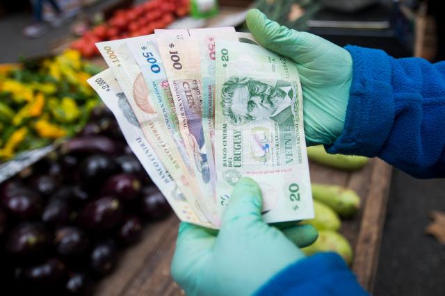 (FILES) A street vendor shows Uruguayan banknotes at a street market in Montevideo on April 23, 2024. Uruguay's economy slowed in 2025 compared to 2024, though it did not slip into negative territory, according to official data released by the Central Bank of Uruguay (BCU) on March 24, 2026. (Photo by Pablo VERA / AFP)