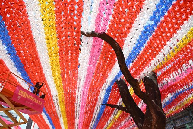 A temple worker attaches name cards with wishes of Buddhist followers to lotus lanterns installed for upcoming celebrations of Buddha's birthday at Jogyesa Temple in Seoul on March 25, 2026. (Photo by Jung Yeon-je / AFP)