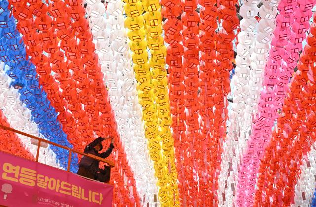 A temple worker attaches name cards with wishes of Buddhist followers to lotus lanterns installed for upcoming celebrations of Buddha's birthday at Jogyesa Temple in Seoul on March 25, 2026. (Photo by Jung Yeon-je / AFP)