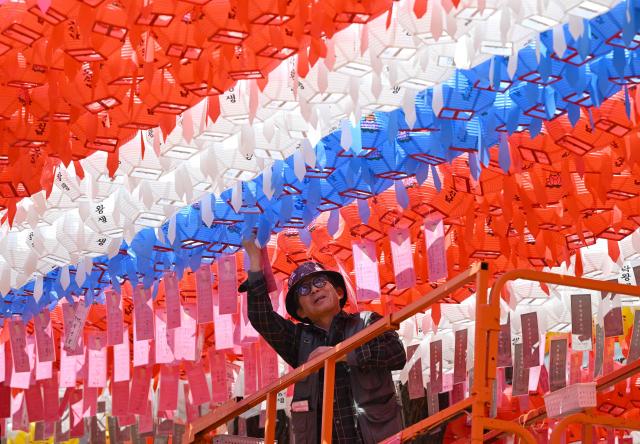 A temple worker attaches name cards with wishes of Buddhist followers to lotus lanterns installed for upcoming celebrations of Buddha's birthday at Jogyesa Temple in Seoul on March 25, 2026. (Photo by Jung Yeon-je / AFP)