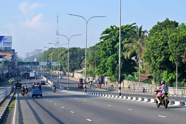 Commuters ride along a deserted street in Colombo on March 25, 2026 after Sri Lanka introduced a four-day work week to conserve fuel reserves amid the Middle East war. Sri Lanka ordered street lights, neon signs and billboard lighting to be switched off from March 24 as part of measures to cut energy consumption by 25 percent to tackle supply shortages. The island brought back work-from-home arrangements since last week, to reduce pressure on the transport network. (Photo by Ishara S. KODIKARA / AFP)